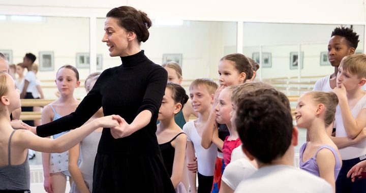 A teacher demonstrating with a student surrounded by a group of young dancers.
